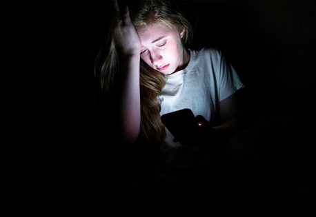 Upset girl sitting in the dark while using her smartphone. The l
